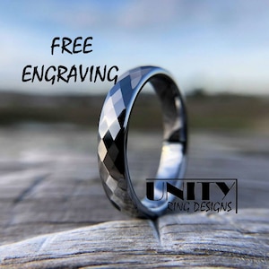 May include: A black tungsten carbide ring with a diamond-shaped pattern. The ring is on a wooden surface. The text "FREE ENGRAVING" is at the top of the image. The text "UNITY RING DESIGNS" is at the bottom of the image.