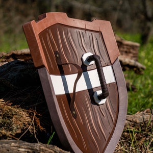May include: A brown and white wooden shield with a leather strap handle. The shield has a wood grain texture and a white stripe across the centre.