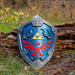 May include: A blue and silver shield with a red and yellow Triforce symbol. The shield is made of plastic and has a realistic look.
