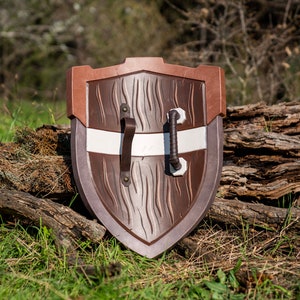 May include: A brown wooden shield with a white stripe and two leather straps. The shield is resting on a log.