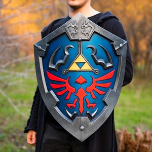May include: A blue and silver shield with a red and yellow winged design. The shield has a triangular symbol with a yellow interior and a black outline.