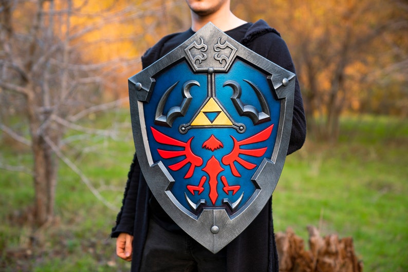 May include: A blue and silver shield with a red and yellow winged design. The shield has a triangular symbol with a yellow interior and a black outline.