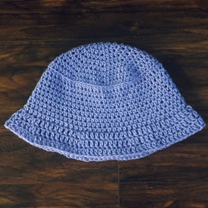 May include: A light purple crocheted bucket hat. The hat is made with a simple stitch pattern and has a wide brim.