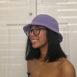 May include: A person wearing a purple crochet bucket hat with black framed glasses.