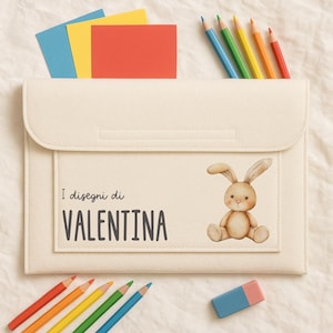 Peut inclure: Pochette en feutre crème avec fermeture à rabat, ornée d'une illustration de lapin et du texte "I disegni di VALENTINA." Des crayons de couleur et du papier sont visibles. Une gomme est également présente.