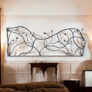 May include: A wrought iron wall decor featuring a stylized design of branches and leaves. The decor is mounted on a white wall above a brown wooden table and a brown wooden nightstand.