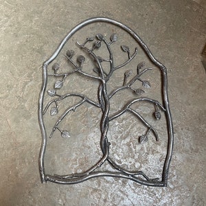 May include: A silver metal wall art piece in the shape of a tree with branches and leaves. The tree is framed by a curved arch.