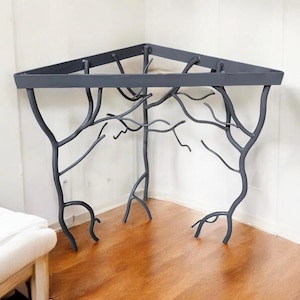 May include: A corner shelf made of black metal with a tree branch design. The shelf is mounted to a wall and has a flat top surface.
