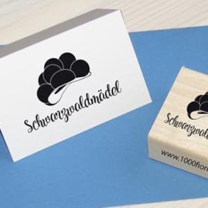 Könnte beinhalten: Ein Holz-Stempel mit dem Text "Schwarzwaldmädel" und einer Schwarz-Weiß-Illustration eines traditionellen Schwarzwälder Hutes. Der Text "www.1000flori.de" ist ebenfalls auf dem Stempel.