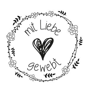May include: Black and white illustration of a wreath with flowers and leaves. The wreath has the text "mit Liebe gewebt" in the center.