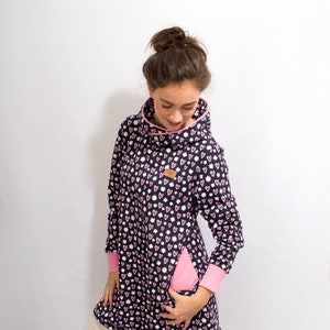 Puede incluir: Un vestido azul marino con capucha con estampado de corazones rosas y blancos. El vestido tiene un detalle de cremallera rosa en el lateral y un cord&oacute;n rosa en la parte inferior. La modelo lleva medias blancas y zapatillas blancas.