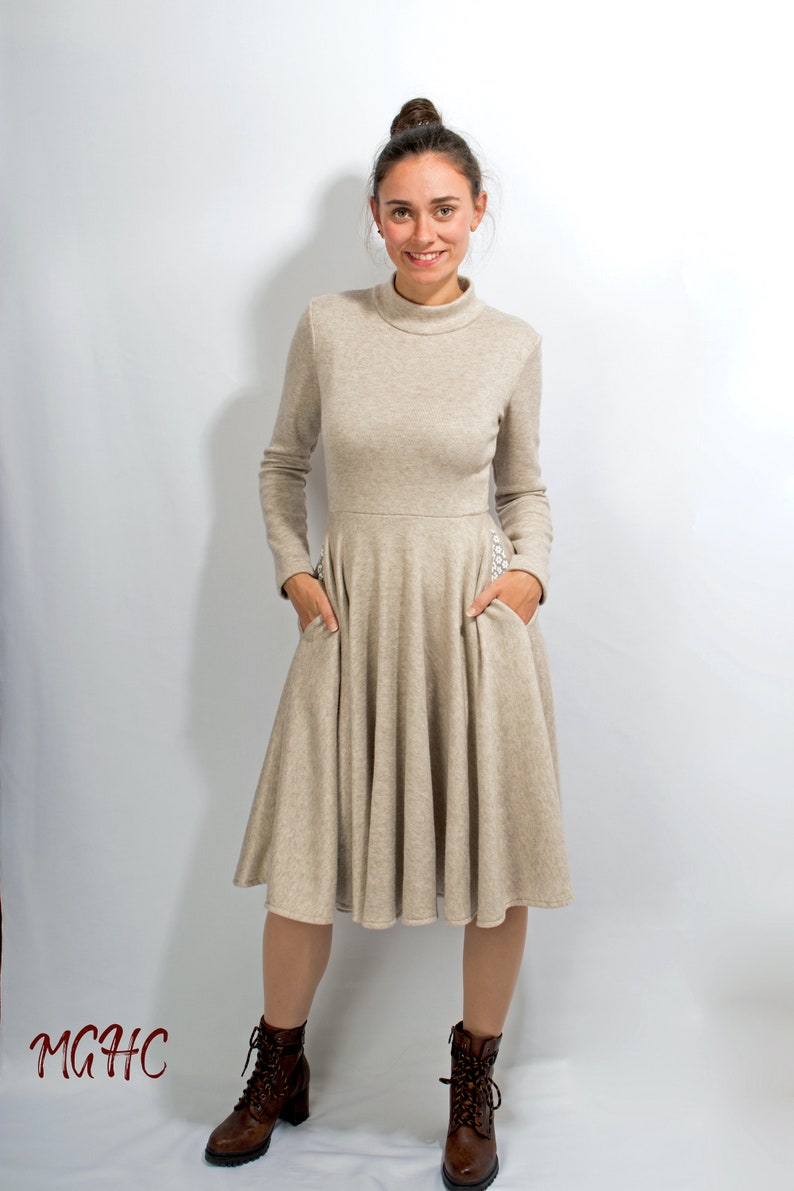 May include: A beige long-sleeved dress with a high neckline and a flared skirt. The dress has pockets on the sides and is made of a soft, comfortable fabric.