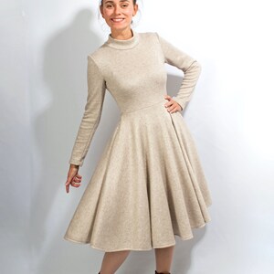 May include: A beige long-sleeved dress with a high neck and a flared skirt. The dress is made of a soft, knit fabric. The model is wearing brown ankle boots.