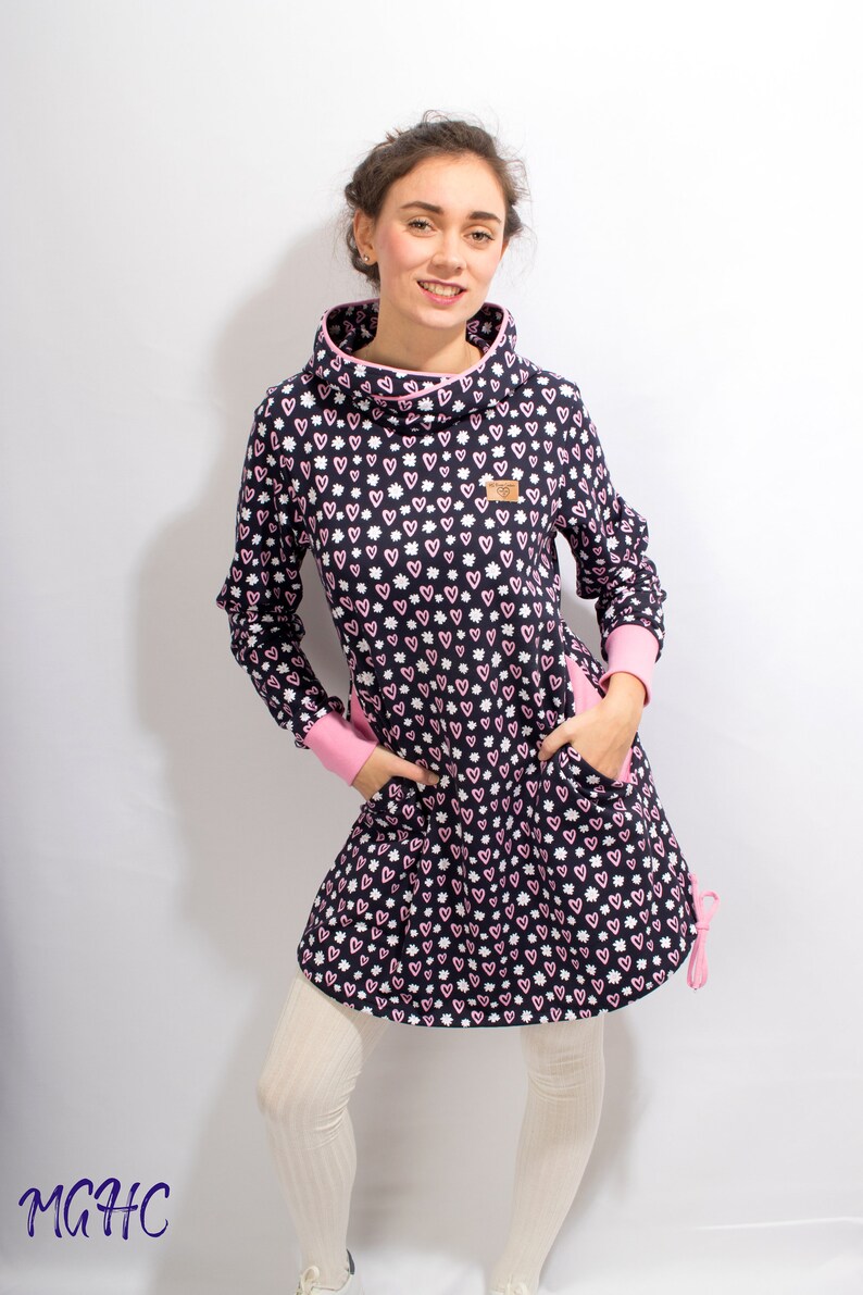 Puede incluir: Un vestido azul marino con un estampado de corazones rosas y blancos. El vestido tiene cuello alto, mangas largas y dos bolsillos. El vestido est&aacute; hecho de una tela suave y c&oacute;moda.