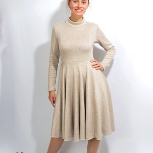 May include: A beige long-sleeved dress with a high neck and a flared skirt. The dress is made of a soft, comfortable fabric and is perfect for a casual or semi-formal occasion.