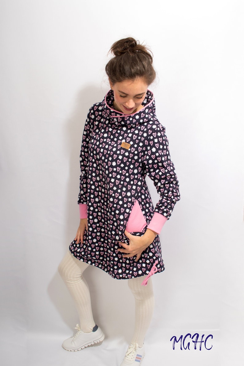 Puede incluir: Un vestido azul marino con capucha con estampado de corazones rosas y blancos. El vestido tiene un detalle de cremallera rosa en el lateral y un cord&oacute;n rosa en la parte inferior. La modelo lleva medias blancas y zapatillas blancas.