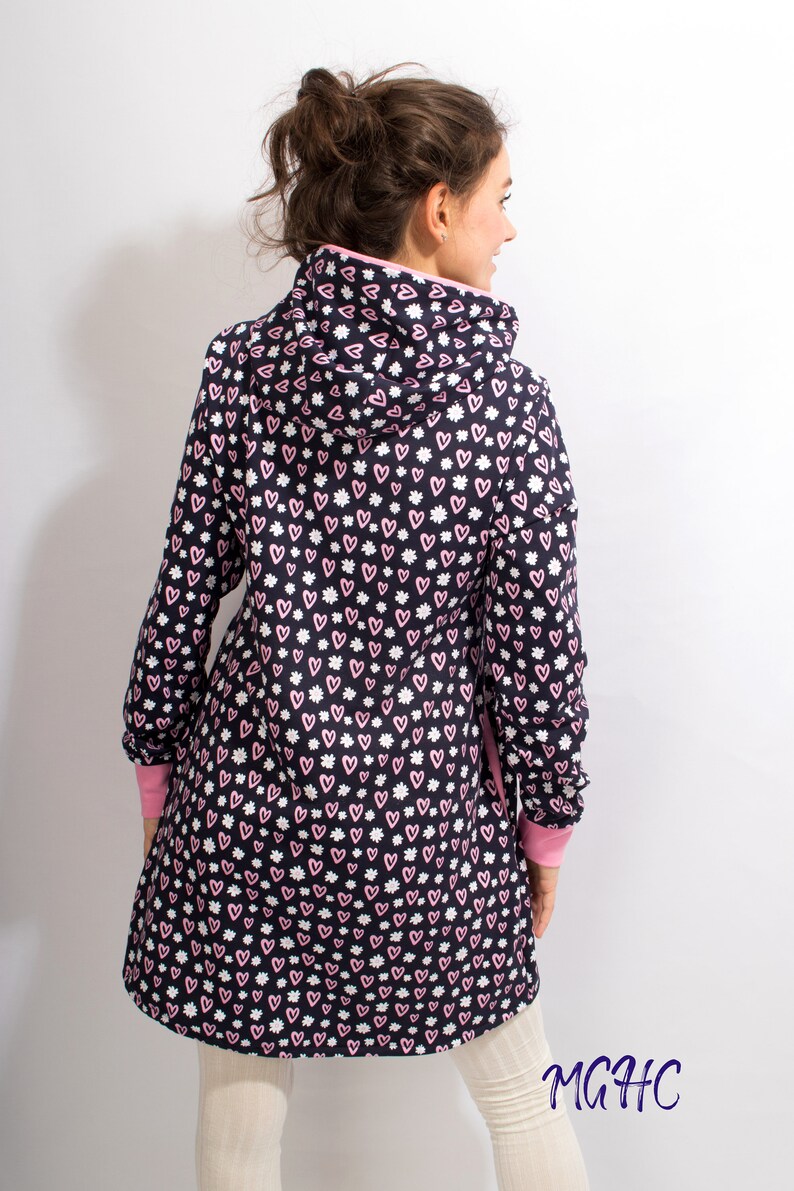 Puede incluir: Una chaqueta con capucha de manga larga con fondo negro y un patr&oacute;n de corazones rosas y flores blancas. La chaqueta tiene un ribete rosa alrededor de la capucha y los pu&ntilde;os.