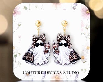 May include: A pair of dangle earrings featuring a white ghost character wearing black sunglasses, a leopard print bow, and carrying a matching leopard print handbag while holding a drink cup with a skull design, attached to gold-tone posts.