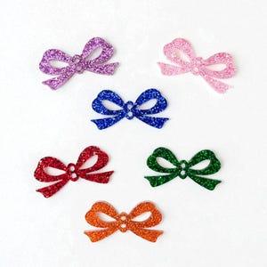 K&ouml;nnte beinhalten: Sechs glitzernde Schleifen in verschiedenen Farben: Lila, Rosa, Blau, Rot, Gr&uuml;n und Orange. Diese dekorativen Schleifen sind auf wei&szlig;em Hintergrund angeordnet und zeigen ihre glitzernde Textur und lebendigen Farbt&ouml;ne.