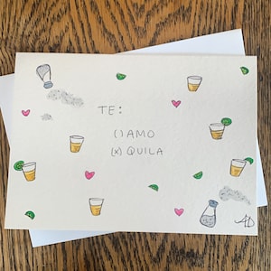 May include: A handwritten card with the text "TE: ( ) AMO (X) QUILA" and illustrations of hearts, glasses, limes, and salt shakers.