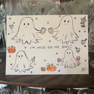 Puede incluir: Una tarjeta de felicitaci&oacute;n blanca con una ilustraci&oacute;n dibujada a mano de cuatro fantasmas sosteniendo varias bebidas alcoh&oacute;licas, incluyendo cerveza, vino y c&oacute;cteles. El texto dice I'M HERE FOR THE BOOS! con calabazas naranjas y puntos.