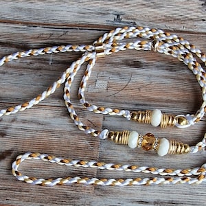 May include: A white and brown braided dog leash with gold beads and a crystal charm.