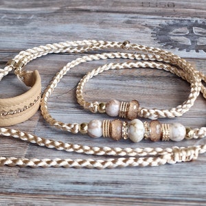 Può includere: Un set di collari per cani in pelle intrecciata beige e un braccialetto abbinato con dettagli dorati e perline bianche e marroni.