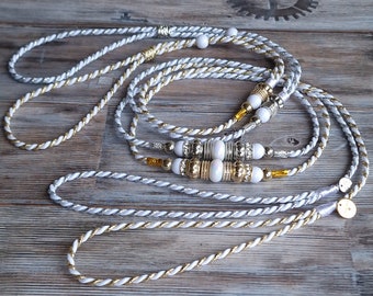 May include: White and gold braided rope with white and gold beads. The rope is twisted and has a decorative knot at the end.