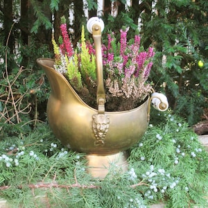 Peut inclure: Un pot en laiton avec un motif de tête de lion et des poignées en porcelaine blanche, rempli de fleurs de bruyère roses et blanches.