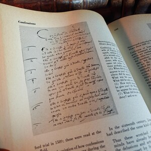 May include: An open book with text and handwritten notes. The page shows the word "Confessions" at the top. The text is in a script font. The book is open to a page with a detailed description of confessions.