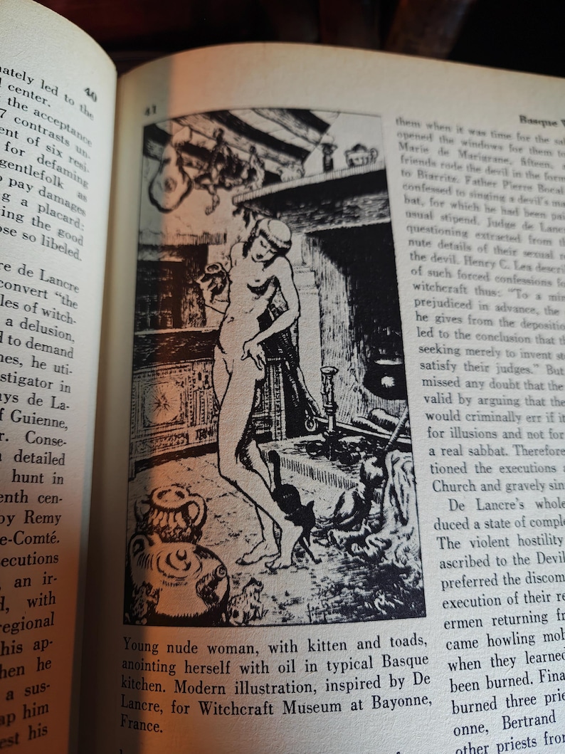 May include: Black and white illustration of a nude woman in a kitchen with a kitten and toads. The image is inspired by De Lancre for the Witchcraft Museum at Bayonne, France.