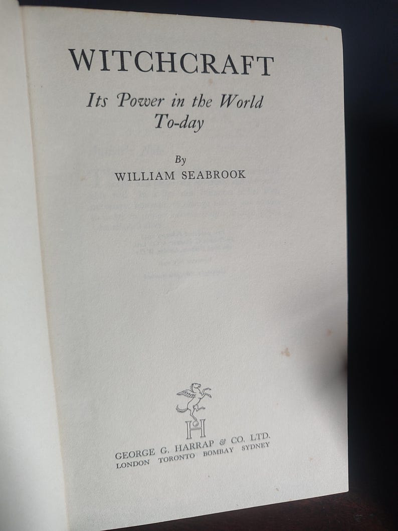 Może przedstawiać: Otwarta książka zatytułowana "WITCHCRAFT" autorstwa Williama Seabrooka. Tytuł jest pogrubiony, z podtytułem "Its Power in the World To-day" poniżej. Nazwisko autora jest wyśrodkowane. Logo i nazwa wydawcy znajdują się na dole.