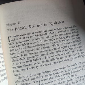 Może przedstawiać: Otwarta strona książki z tytułem "The Witch's Doll and its Equivalent". Tekst opisuje praktyki czarownic z użyciem lalek, w tym przebijanie ich gwoździami lub igłami. Strona pochodzi z książki.