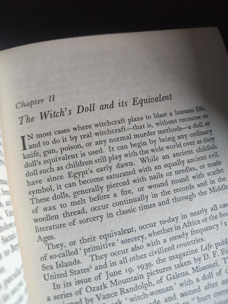 Może przedstawiać: Otwarta strona książki z tytułem "The Witch's Doll and its Equivalent". Tekst opisuje praktyki czarownic z użyciem lalek, w tym przebijanie ich gwoździami lub igłami. Strona pochodzi z książki.