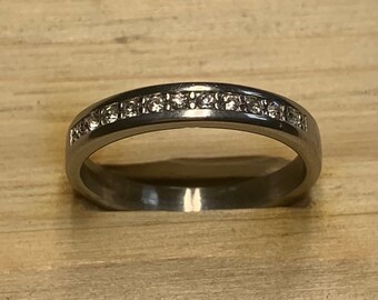 May include: A silver band ring with a row of small clear stones set in the band.