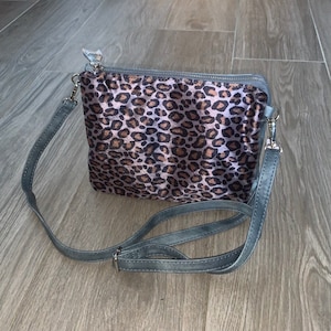 May include: A grey and brown leopard print crossbody bag with a silver zip and a grey adjustable strap.