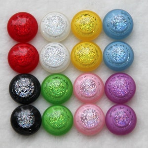 Könnte beinhalten: Sortiment von 12 runden, flach geformten Knöpfen mit Glitzerakzenten. Die Knöpfe sind in verschiedenen Farben, darunter Rot, Weiß, Gelb, Blau, Grün, Rosa und Schwarz.
