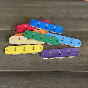 May include: A collection of colorful wooden key holders, each with a different number from 1 to 9. The key holders are in various colors, including red, blue, green, yellow, and purple. Each holder has small holes for keys.