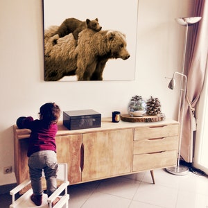 May include: A sepia-toned photograph of a brown bear and a cub. The bear is standing on all fours and the cub is sitting on its back. The photograph is framed and hanging on a white wall.