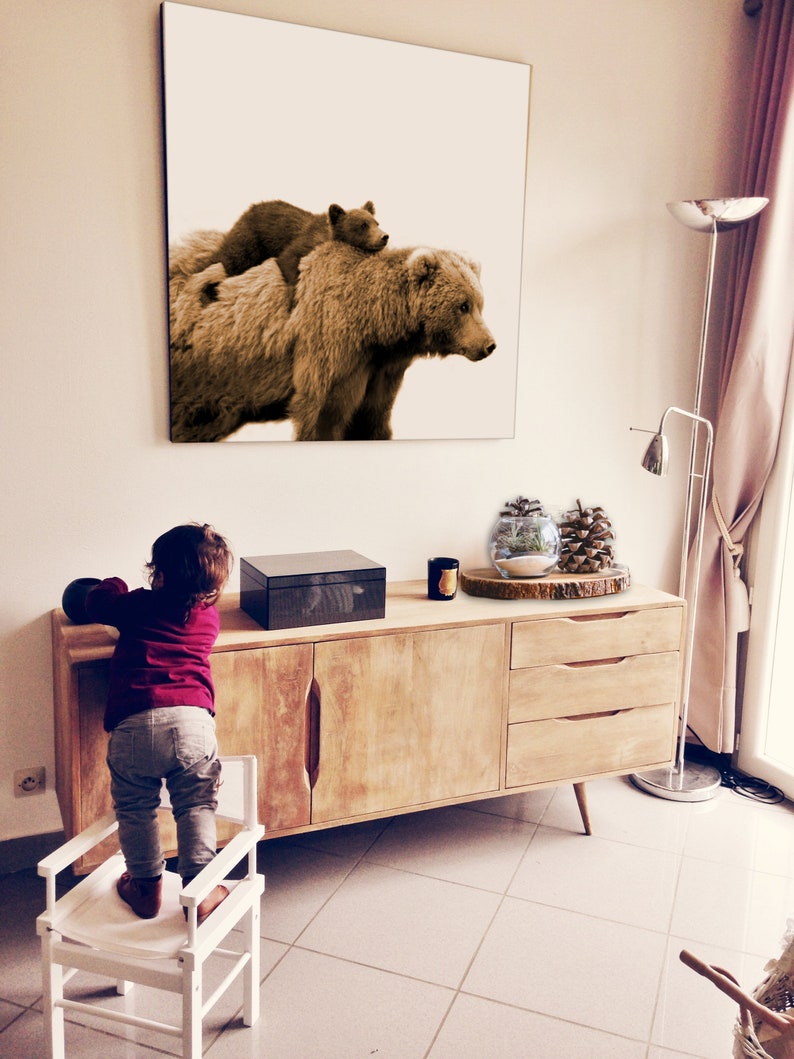 May include: A sepia-toned photograph of a brown bear and a cub. The bear is standing on all fours and the cub is sitting on its back. The photograph is framed and hanging on a white wall.