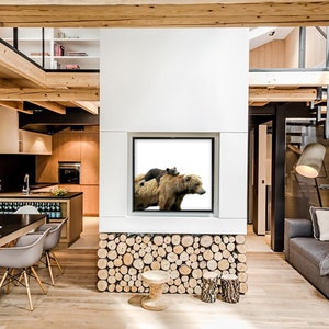 May include: A modern living room with a large picture of a brown bear and a cub on a white background hanging on the wall. The room has a wooden floor, a black dining table, and a gray couch.