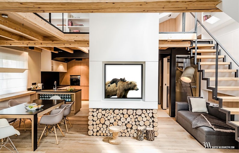 May include: A modern living room with a large picture of a brown bear and a cub on a white background hanging on the wall. The room has a wooden floor, a black dining table, and a gray couch.