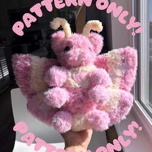 May include: A plush moth toy made of pink and cream-colored faux fur with two antennae, a heart-shaped patch on the chest, and star-shaped accents on the wings. The text PATTERN ONLY is printed in pink letters at the top and bottom of the image.