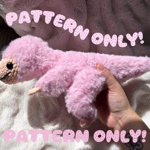 May include: A plush pink dinosaur toy with a fuzzy texture, a crocheted face, and black eyes. The text "PATTERN ONLY!" is displayed in pink letters at the top and bottom of the image, indicating that this is a digital design guide.