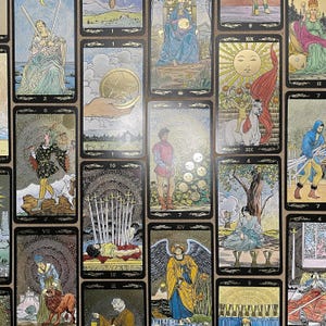 May include: A collection of tarot cards with various illustrations. The cards feature images of figures, symbols, and scenes, including a woman with swords, a hand holding a coin, and a figure with wings. The cards have a black border and gold accents.