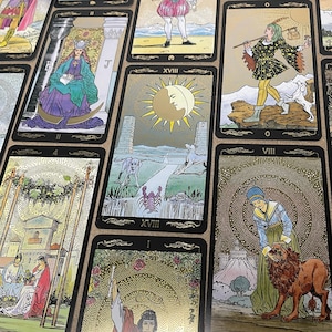May include: A collection of tarot cards with detailed illustrations. The cards feature images of figures, animals, and celestial bodies in a vintage style. The color palette includes gold, black, and various earth tones, creating a mystical aesthetic.