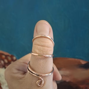 Op de afbeelding: Een set van drie gouden duimringen. De ringen zijn gemaakt van dun, gehamerd metaal en zijn ontworpen om te worden gedragen aan de duim. De ringen zijn op elkaar gestapeld, met de grootste ring onderaan en de kleinste ring bovenaan.