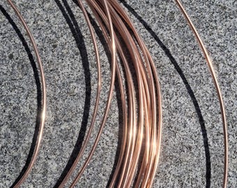 May include: Coiled copper wire, a reddish-brown color, is arranged in a circular pattern. The wire is shiny and reflects light, creating highlights. The background is a gray, textured surface.