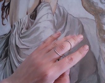 May include: Two silver rings on a finger. The rings are simple and delicate, with a slightly textured finish.