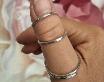 May include: Three thin, silver-colored metal rings with a smooth, polished finish. Two of the rings are positioned on the upper part of the thumb, while the third, slightly larger ring is worn at the base of the thumb, encircling the digit.